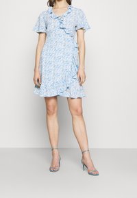 Ljust blå blommig klänning med volanger, korta ärmar och utsvängd nederdel. Har en omslagsdesign och är matchad med exakt samma klackar.