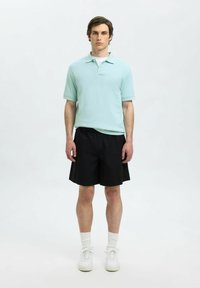 Mintgrön polotröja med kort ärm, i kombination med svarta shorts. Modellen bär vita sneakers och ankelsockor. Enkelt, avslappnat outfit.