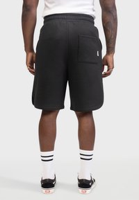 Shorts en coton noirs avec une taille élastique, des poches latérales et une poche arrière en patch. Présente un design épuré et minimaliste.
