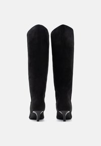 Μπότες από μαύρο σουέντ μέχρι τους μηρούς με εφαρμοστή σιλουέτα, μυτερή μύτη και λεπτό τακούνι. Λεία υφή με ελάχιστες ραφές.