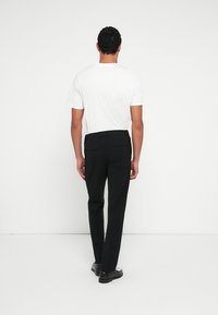 Wit t-shirt met korte mouwen gecombineerd met zwarte zakelijke broek, uitgevoerd in een rechte pasvorm met achterzakken. Draagt donkere schoenen.