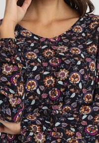 Blusa nera a fiori caratterizzata da una varietà di fiori e foglie colorate. Materiale con una texture e una finitura morbida. Collo a V con maniche ampie.