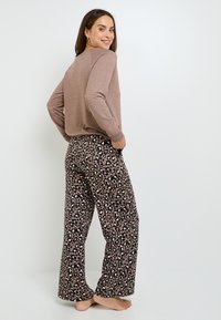 Haut à manches longues marron avec des poignets côtelés, associé à un pantalon large à imprimé léopard présentant un mélange de motifs marron, noir et blanc.