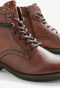 Brown leather ankle boots feature a rounded toe, metal eyelets, decorative studs, and a side zipper for easy access. Textured surface.