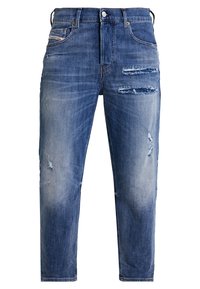 Jean en denim bleu avec une coupe décontractée, comportant des détails effilochés, un léger délavage et un design à cinq poches. Fermeture classique par bouton et zip.