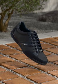 Black sneaker with smooth synthetic material, lace-up design, cushioned collar, and subtle white branding. Lightweight with rubber sole accents.