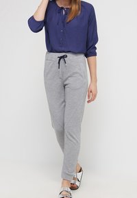 Mörkblå blus med slipskrage och knappdetaljer, kombinerad med ljusgrå, strukturerade joggerbyxor med dragsko i midjan och snedställda fickor.
