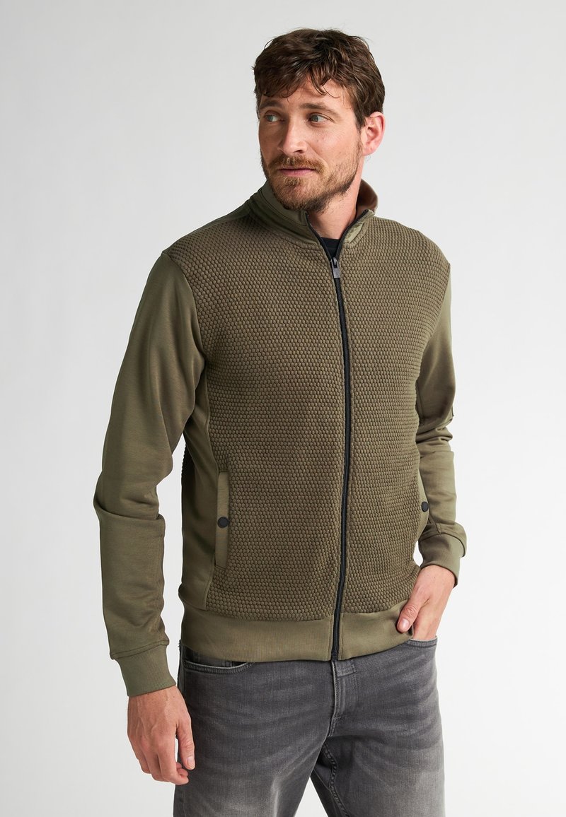 Olivengroen zip-up jack met een textuur aan de voorzijde, gladde mouwen, ritszakken en geribbelde manchetten. Het ontwerp heeft een hoge kraag en een getailleerde vorm.