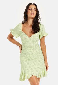 Short green dress with dotted pattern, puff sleeves, fitted bodice, and flared hem. Soft fabric with slight sheen and ruffled accents.