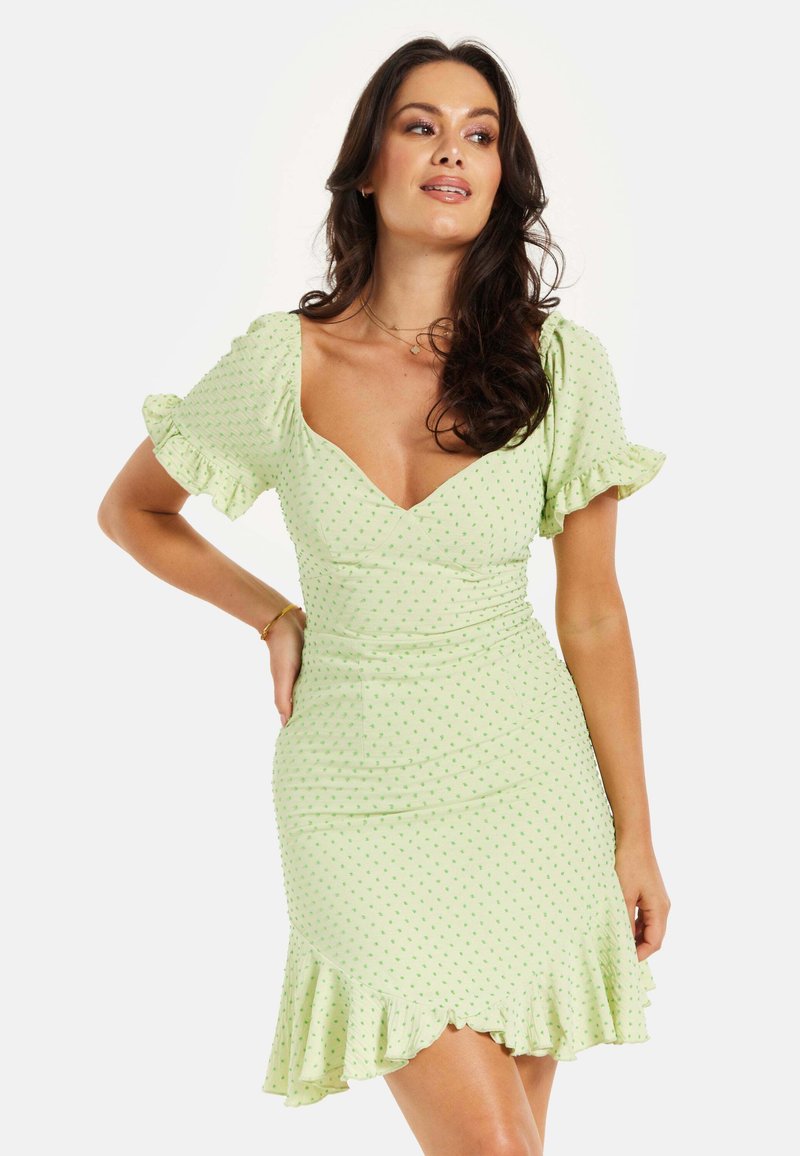 Short green dress with dotted pattern, puff sleeves, fitted bodice, and flared hem. Soft fabric with slight sheen and ruffled accents.