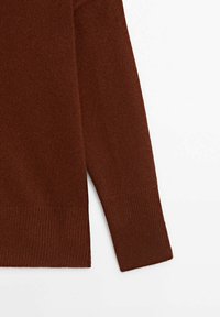 Pull en maille brun avec des manches longues, des poignets côtelés et des fentes sur les côtés. Texture lisse et design minimal.