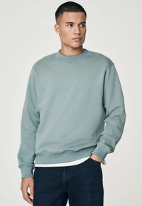 Sudadera azul clara con cuello redondo, puños y dobladillo acanalados. Hecha de una tela suave, presenta un ajuste relajado y un diseño minimalista.