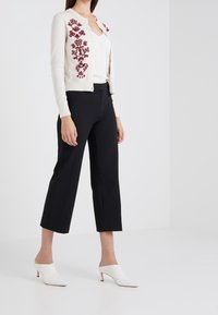 Ivoire cardigan dengan bordir floral burgundy, dipadukan dengan celana cropped hitam. Mules bertumit putih melengkapi penampilan ini.