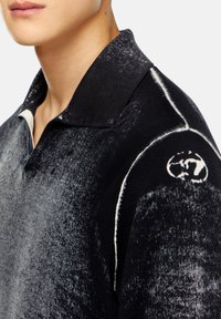Polo noir avec un motif texturé, comprenant un col côtelé, des accents blancs et un logo circulaire sur l'épaule.