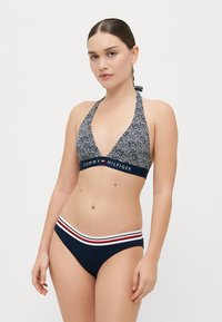 Set bikini blu navy con top a halter decorato e fascia con brand, abbinato a slip con dettagli a strisce rosse e bianche.