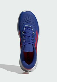 Blue athletic shoe with a breathable mesh upper, red accents, flat laces, and a textured white sole featuring black speckles.