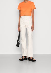 Orange cropped t-shirt, hvide høj talje lige bukser, sorte flade sandaler og en lille sort taske.
