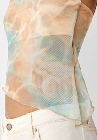 Top trasparente in morbido pesca chiaro con motivi tie-dye blu e verde acqua. L'orlo è asimmetrico. Il tessuto ha una finitura liscia, leggermente strutturata.