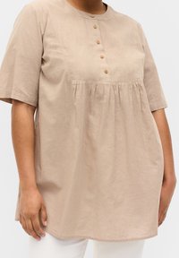 Beige, short-sleeved tunic made of linen, featuring a round neckline with eight wooden buttons and a gathered waist detail.
