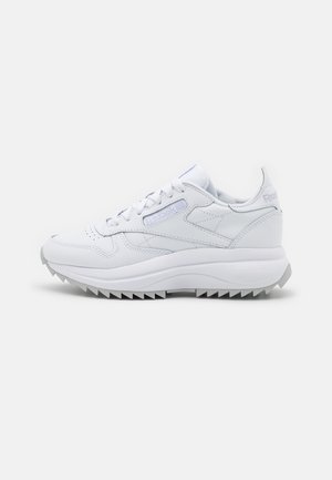 Baskets blanches en cuir Reebok avec semelle dentelée, logo sur le côté et le talon, et lacets blancs, vues de côté extérieur sur fond blanc.