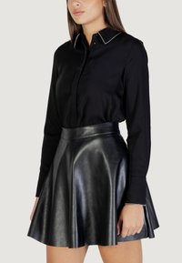 Camicia nera a maniche lunghe con colletto strutturato e cuciture bianche, abbinata a una gonna nera in pelle a vita alta e svasata.