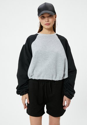 Sudadera en bloques de color gris y negro con mangas raglán, combinada con shorts negros. El material parece suave con un ajuste relajado.