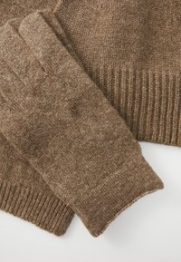 Guanti in maglia marrone con una texture morbida, dotati di polsini a costine e una finitura liscia e calda. Il tessuto mostra leggere variazioni di colore.