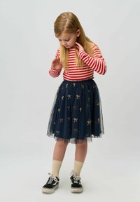 Un top de rayas rojas y blancas de manga larga combinado con una falda de tul azul marino con patrones de lazos dorados. Zapatillas negras con cordones blancos.