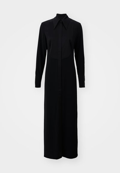 Crna haljina dugih rukava s dugmadi sprijeda, klasičnom ovratniku i ravnim siluetom, izrađena od glatkog materijala.