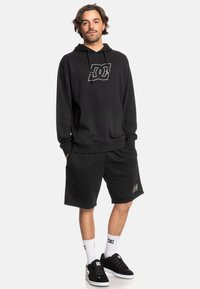 Sudadera negra con un logo, combinada con pantalones cortos negros. El conjunto está hecho de una tela suave, con un ajuste relajado y diseño con cordón.