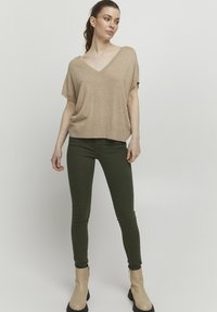 Beige pletený top s výstřihem do V, kombinovaný s přiléhavými tmavě zelenými džíny a krémovými kotníkovými botami s černou podrážkou. Hladké textury, uvolněný střih.