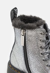 Zilveren veterschoenen met een gebroken leren patroon, een zwart leren kraag met bontvoering en een zijrits voor sluiting. Rubberen zool.