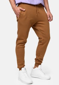 Brune bomulds joggers med en tapered design, elastisk talje, og sidelommer, parret med hvide sneakers.