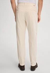 Kremowe spodnie sztruksowe o teksturowanej powierzchni, z dwoma tylnymi kieszeniami i elastyczną talią. Połącz je z ciemnobrązowymi butami.