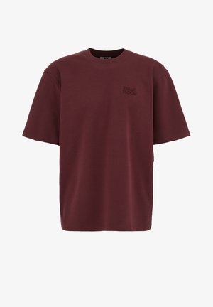 T-shirt oversize à manches courtes couleur bordeaux avec col ras du cou et petit logo "Urban Bloom" brodé sur le côté gauche de la poitrine.