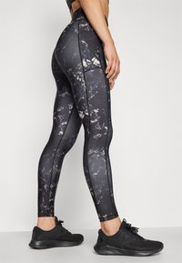 Black leggings with a marble pattern featuring shades of gray and white, made of stretchy material, paired with black athletic shoes.