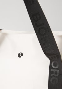 Bolso tote blanco con textura suave, con un logo negro y una correa negra grabada con "BJÖRN BORG". Diseño minimalista.