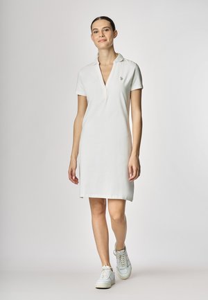 Vestito polo bianco con maniche corte, scollatura a V e piccolo dettaglio del logo. Abbinato a sneakers bianche, tessuto morbido e taglio dritto.