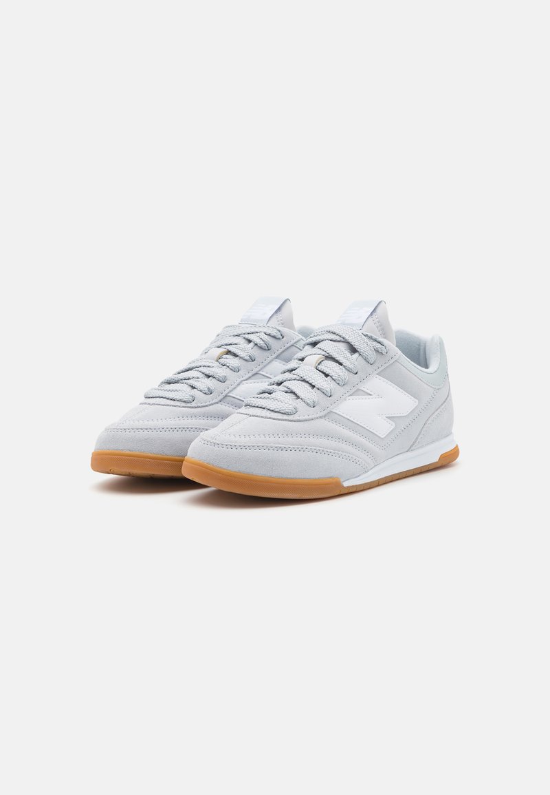 Des chaussures de sport en suède gris avec un logo blanc, dotées de lacets texturés, d'une semelle en caoutchouc gomme et d'un design profil bas.
