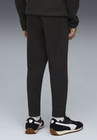 Zwarte sweatpants met een taps toelopend ontwerp, voorzien van textuurpanelen en zijzakken, gecombineerd met zwarte sneakers met witte accenten.