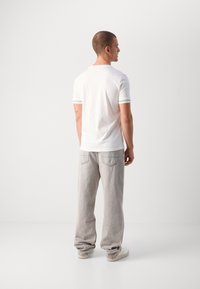 Polo shirt bianco a maniche corte con polsini a righe a contrasto, abbinato a jeans grigi larghi. Modello di spalle, che mostra il design dell'abbigliamento.