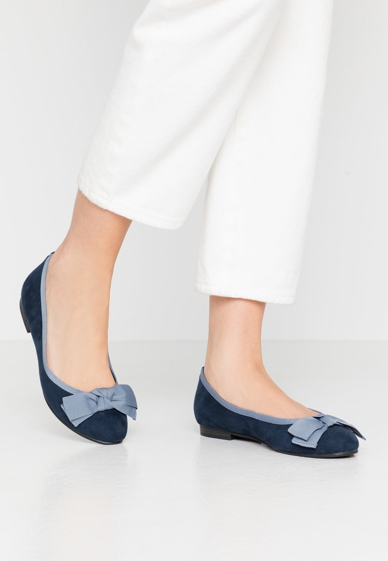 Ballerines en suède bleu marine avec un noeud en ruban bleu clair, bout arrondi et petit talon. La partie supérieure présente une bordure de contraste.