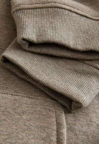 Lysebrunt sweatshirtstof med ribbede manchetter og kant, som viser en blød tekstur og et subtilt, meleret mønster.