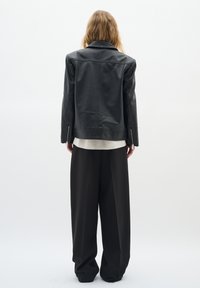 Jachetă din piele neagră cu un design cu guler, manșete cu fermoar și o textură netedă, asortată cu pantaloni negri largi.