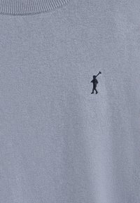 Pull bleu clair en tricot doux, avec un col rond côtelé et un petit emblème sombre représentant une silhouette tenant un bâton.