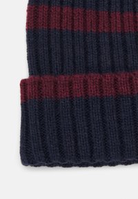 Trakač beanie u tamnoplavoj boji s bordo prugama. Ima rebrastu teksturu i preklopni rub na dnu. Topao i rastezljiv materijal.
