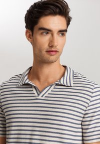 Polo a maniche corte con colletto in crema con strisce blu navy, caratterizzato da un scollo a V e tessuto testurizzato per un look moderno.