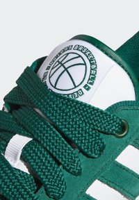Zelena nubuk košarkaška cipela s teksturiranim zelenim vezicama, bijelim detaljima, kružnim logom na jeziku i mrežastim naglascima.