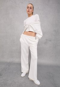 Witte cropped sweatshirt met rits, gecombineerd met losse witte sweatpants. Gladde stof, casual ontwerp en elastische tailleband. Witte sneakers.