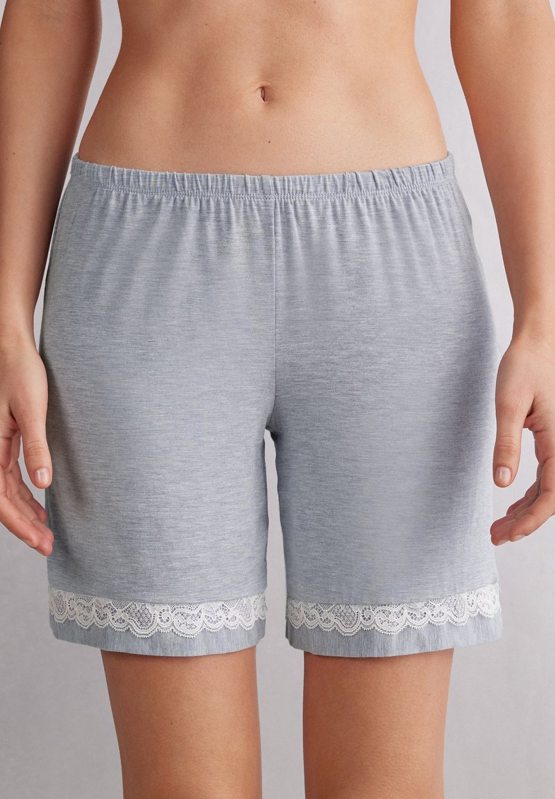 Lichtgrijze katoenen shorts met een elastische tailleband, voorzien van een decoratieve witte kantafwerking aan de zoom. Zacht, relaxte pasvorm, knielang.